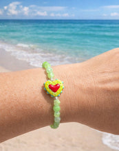 Load image into Gallery viewer, Peridot 10 Breaths Bracelet with a heart charm on a wrist by the ocean