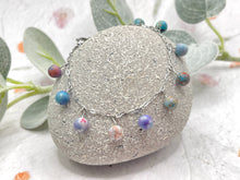 Load image into Gallery viewer, Bracelet with colorful lilac and blue sea sediment jasper stones on a stone surface with greenery in the background
