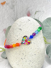 Load image into Gallery viewer, Rainbow colours beaded bracelet with a heart-shaped multicolored charm on a stone surface.
