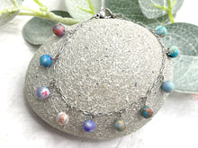 Load image into Gallery viewer, Bracelet with colorful lilac and blue sea sediment jasper stones  on a stone surface with greenery in the background

